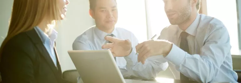 Three business professionals discussing work at a table with a laptop.