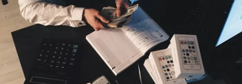 Person counting money at a desk with phones and a notebook.