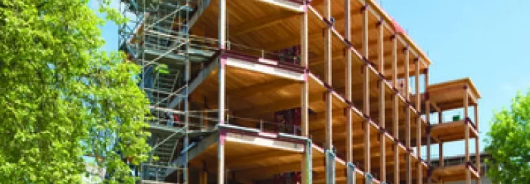 Partially constructed building with scaffolding and cranes under a blue sky.