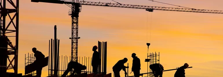 Silhouettes of construction workers and a crane at sunset.