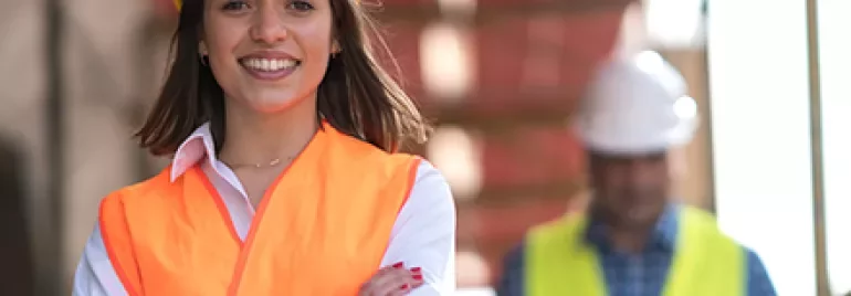 Smiling woman in a construction helmet and safety vest, standing confidently.