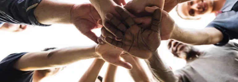 Diverse group of people in a circle with hands stacked in unity.