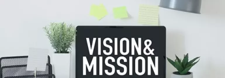 Laptop on desk with 'Vision & Mission' on screen.