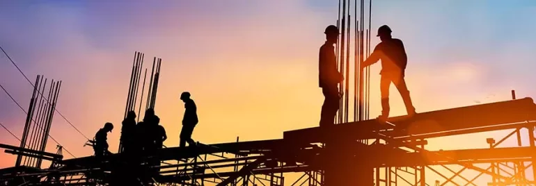 Silhouetted construction workers on scaffolding at sunset