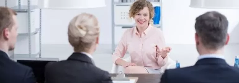 Woman smiling during a job interview with a panel of interviewers in an office.