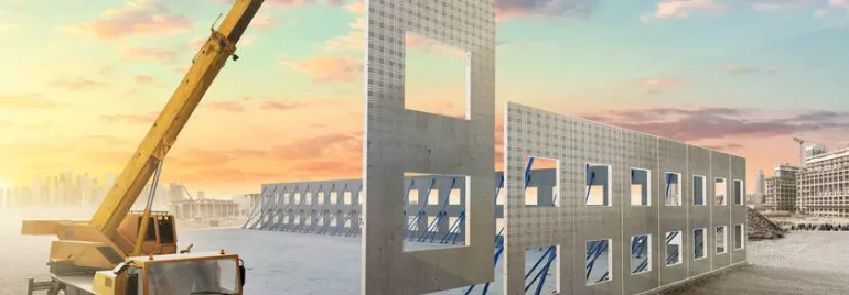 Crane lifting a concrete wall panel at a construction site during sunset.