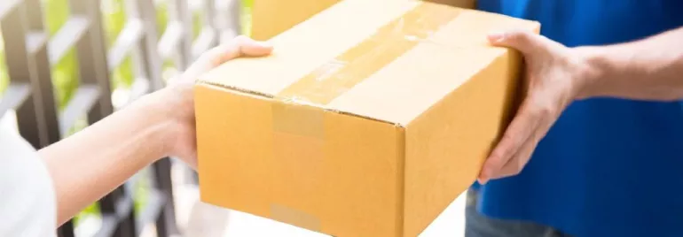 Person in blue shirt handing over a cardboard box outdoors.