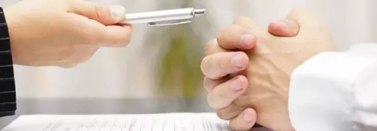 Two people sitting at a desk, a contract and pen in focus.