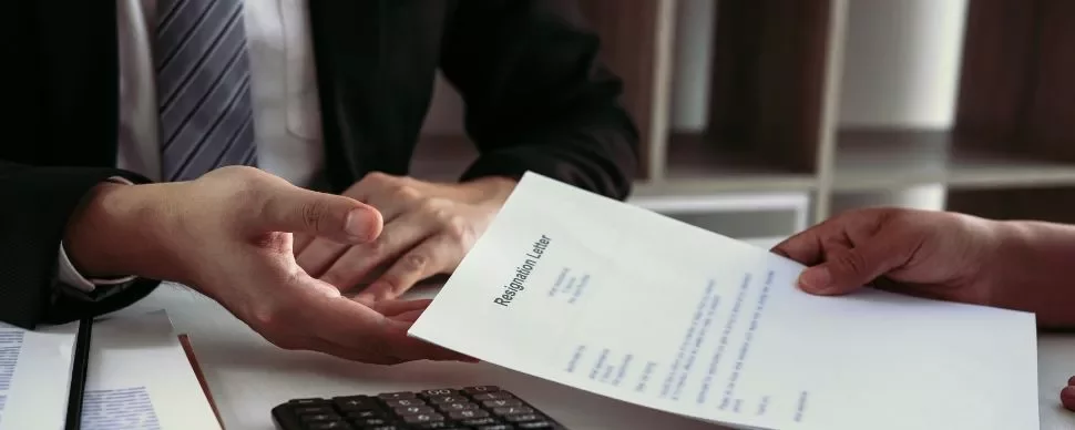 Person handing over a resignation letter across a desk