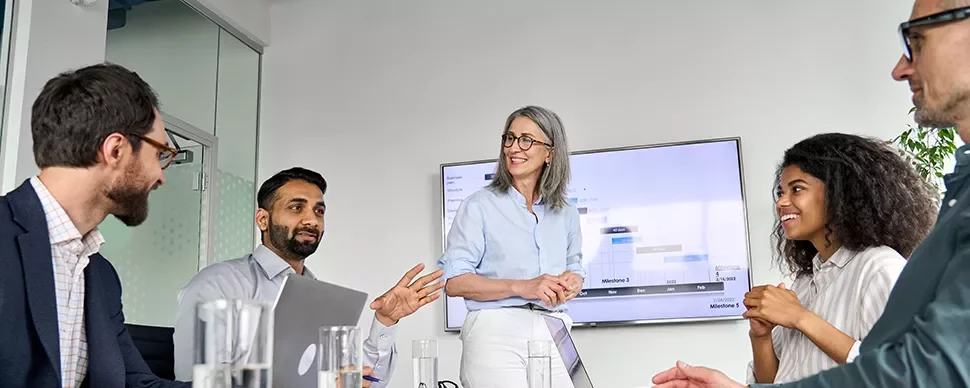 A diverse group of professionals in a meeting room discussing and smiling.