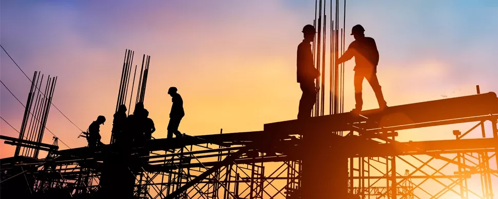 Silhouette of construction workers on scaffolding at sunset.