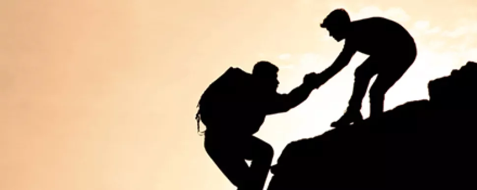 Silhouette of two climbers helping each other on a rocky cliff.