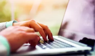 Person typing on a laptop at a desk, close-up view of the hands and keyboard.