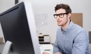 Man with glasses working on a computer in a modern office.