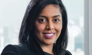 Person smiling in an office setting with a city view in the background.