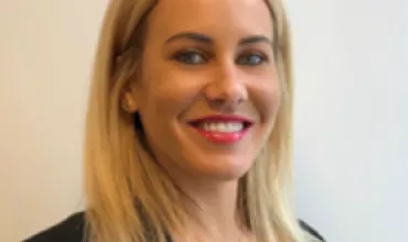 Smiling woman with blonde hair and black blazer against white background.