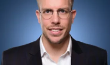 Man in a suit and glasses with a blue background.