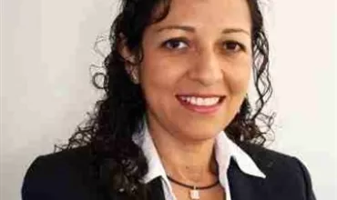 Smiling woman with curly hair wearing a black blazer and white shirt.