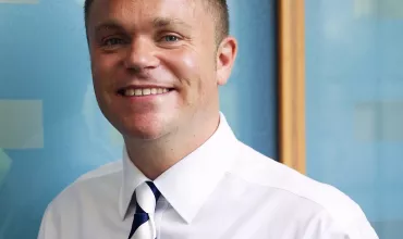 Smiling person in a white shirt and tie against a blue background.
