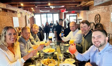 Group of friends enjoying drinks at a table in a cozy restaurant with brick walls.
