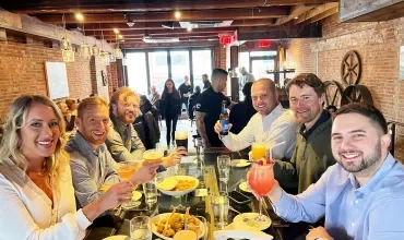 Group of friends enjoying drinks at a table in a cozy restaurant with brick walls.