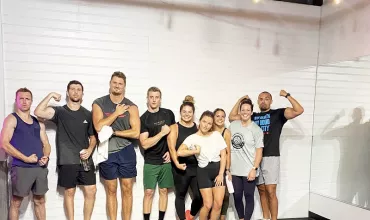 Group of eight people in sporty attire posing in front of a white wall.