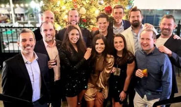 Group of people smiling in front of a decorated Christmas tree.