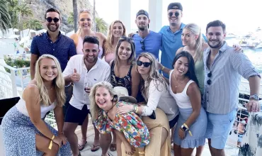 Group of friends smiling and posing on a balcony with a seaside view.
