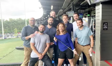 Group of people posing together with golf clubs at a driving range.