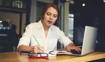 Woman writing notes and using a laptop at a cafe.