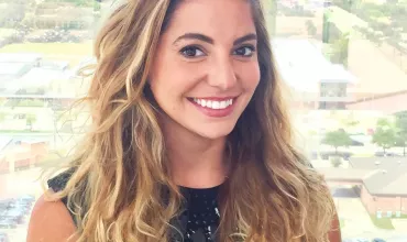 Smiling woman with long curly hair standing in front of a cityscape view.