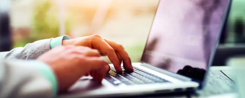 Person typing on a laptop at a desk, close-up view of the hands and keyboard.