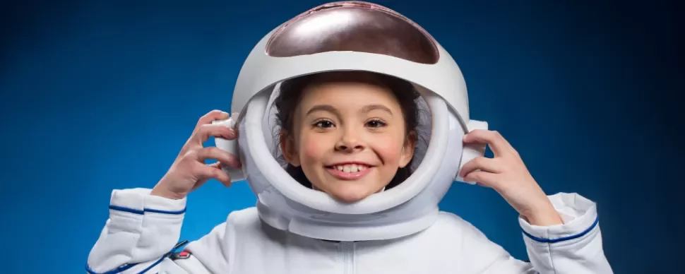 Smiling child wearing an astronaut helmet against a blue background.
