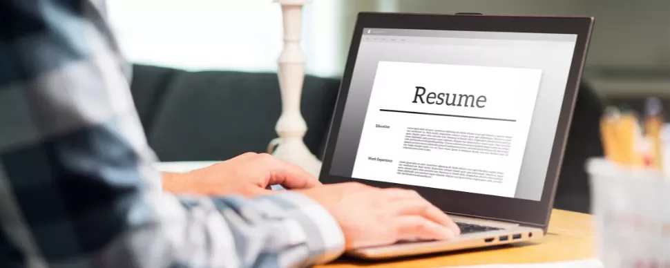 Person writing a resume on a laptop in a home setting.
