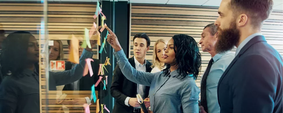 Business team collaborating with sticky notes on glass wall.