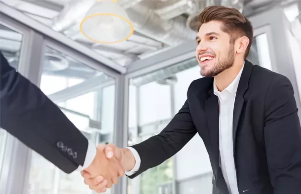 Smiling man in a suit shaking hands with another person in an office setting.