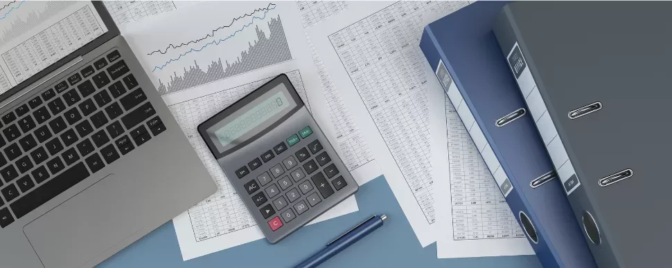 Laptop, calculator, and files on a desk with financial charts and documents.