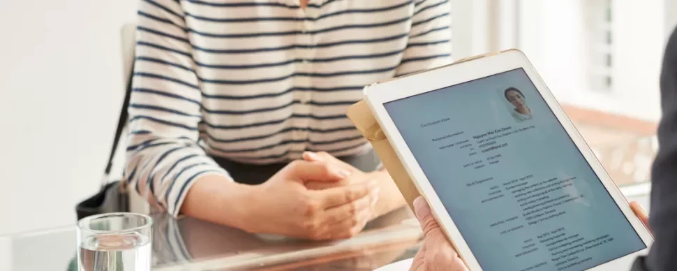 Person holding a tablet showing a resume during an interview at a glass table.