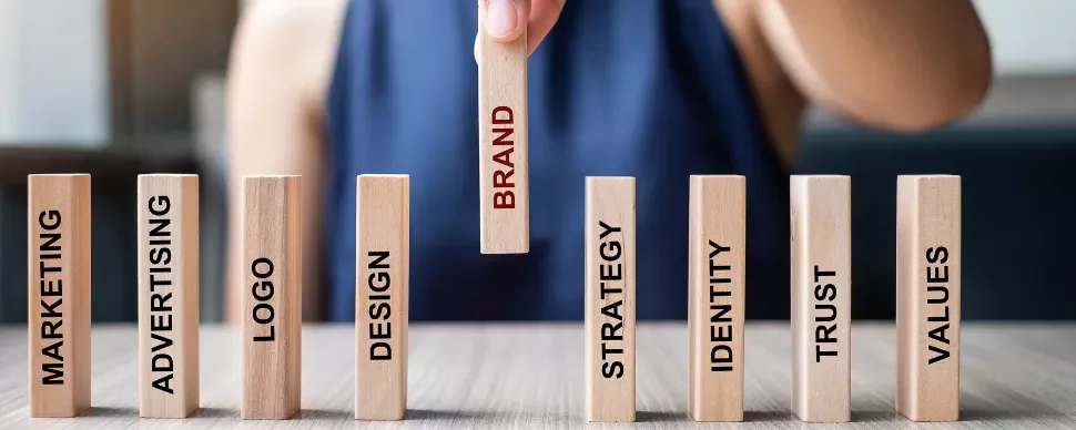Hand holding a block with the word 'Brand' among other business-related blocks on a table.