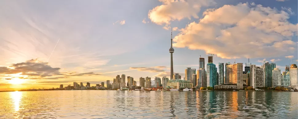 Panoramic view of a city skyline with a tall tower at sunset, reflecting on the water.