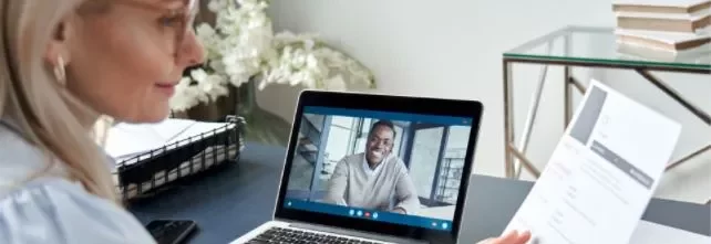 Woman holding a resume during a video call with a man on a laptop.