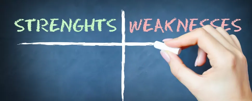 Hand holding chalk writing 'STRENGHT'S' and 'WEAKNESSES' on a board.