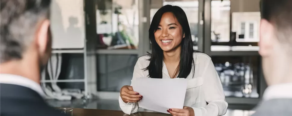 Smiling woman in a white blouse holding papers during a meeting.