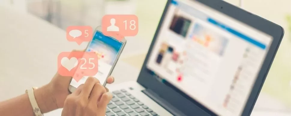 Person using smartphone with social media notifications near a laptop.