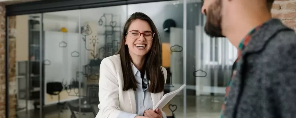 Smiling woman in glasses shaking hands in an office setting.