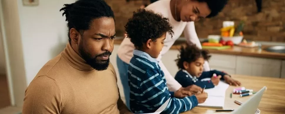 Family working together at a kitchen table with a laptop and books.
