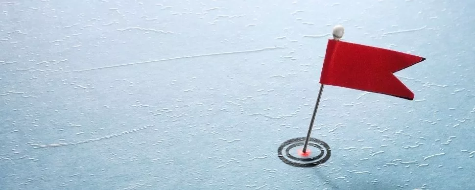 A red flag pin on a textured blue surface resembling ice.