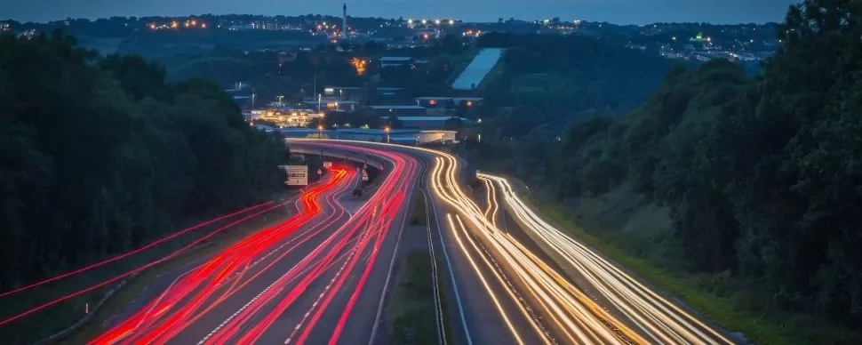 Night view of highway with light trails from vehicles under a dark, starless sky.