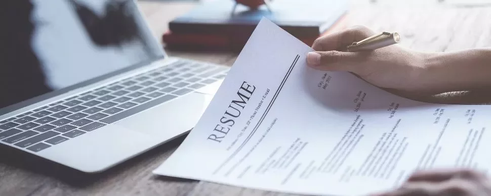 Person reviewing a resume near a laptop.