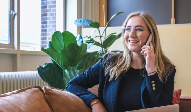 Woman smiling while talking on the phone, seated on a couch.